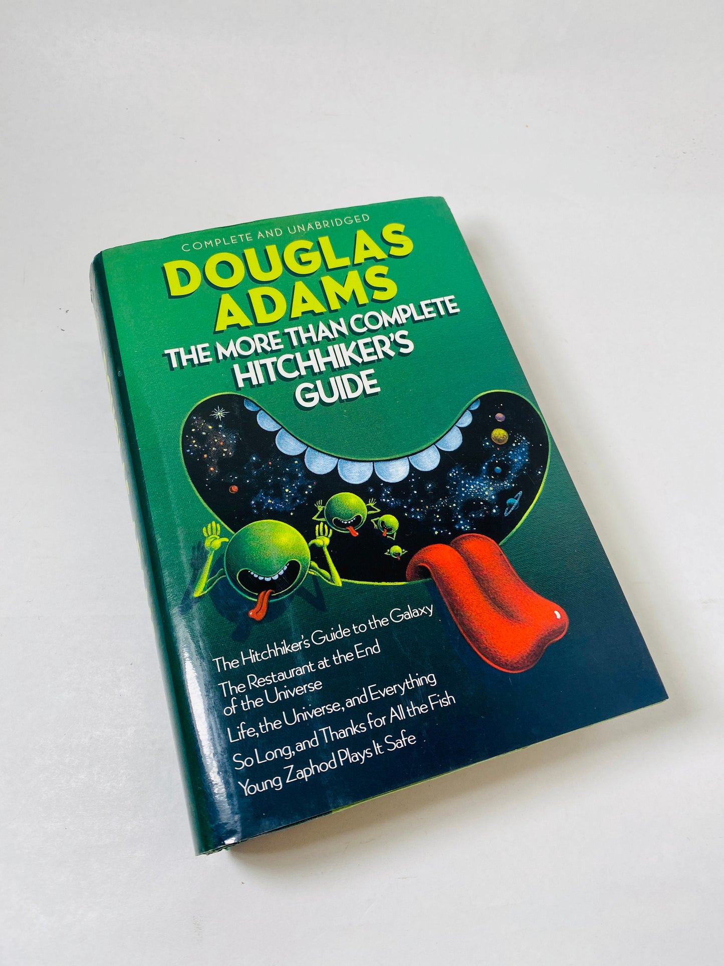Vintage 1989 edition of *The Hitchhiker's Guide to the Galaxy* by Douglas Adams. Complete and unabridged, this book is part of 'A Trilogy in Five Parts.' Cover features whimsical space-themed artwork, capturing the humor and adventure of the series.